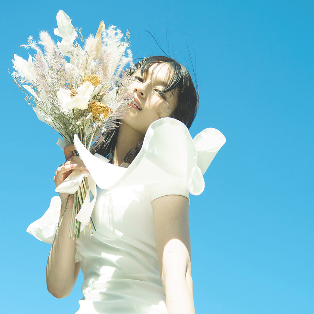 青空を背景に、ブーケを持ったウエディングドレスの花嫁