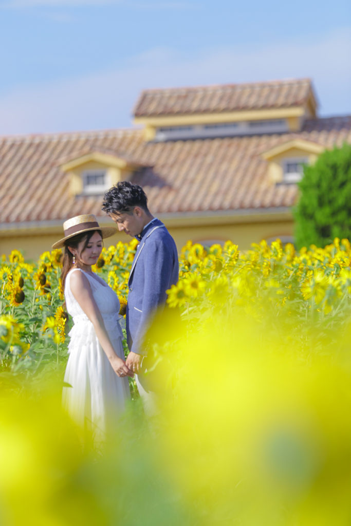 ヒマワリだたけでストローハットをかぶった花嫁、向き合い手をつなぐ花婿