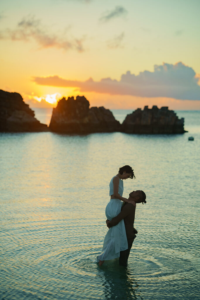 沈む夕陽を背景に、海の中で新婦様を抱っこ