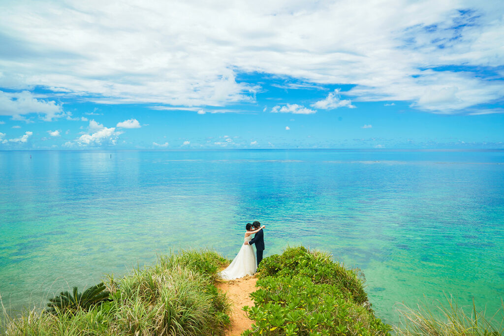 沖縄ブルーの海を背景に、崖の上で向き合う新郎新婦