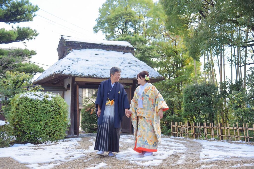 雪の積もった庭園前で和装の新郎新婦が手をつないでいる