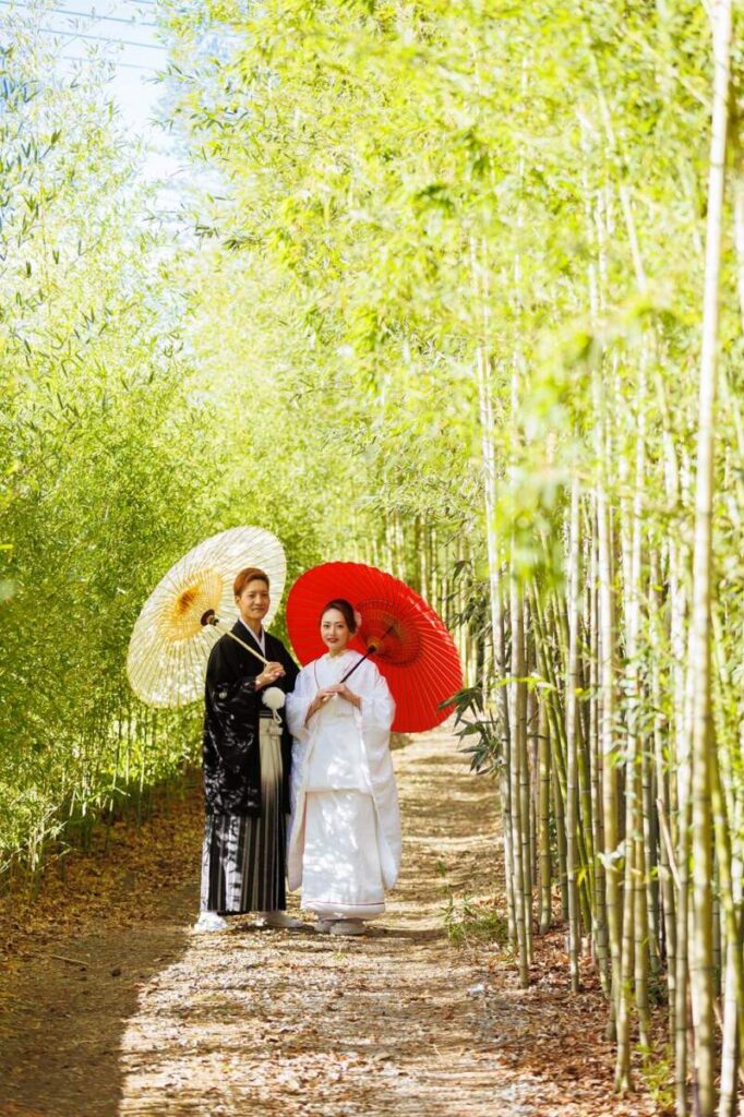 青空と竹林を背景に、紅白の番傘が映える寄り添った新郎新婦。