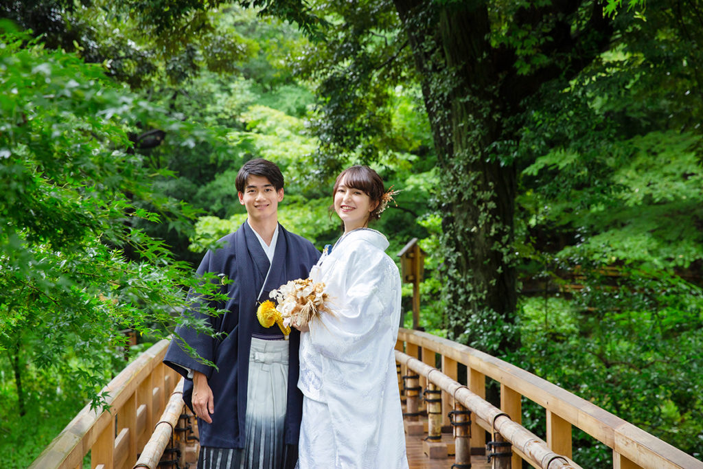 日本庭園の緑の中　橋の上に白無垢と紺紋付の新郎新婦